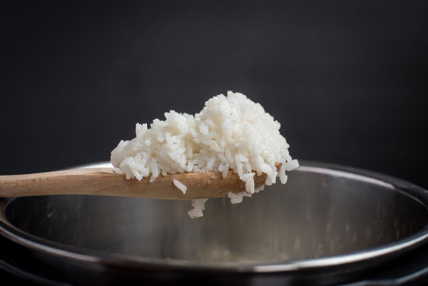 White rice on a wooden spoon, coming out of the Instant Pot cooking pot