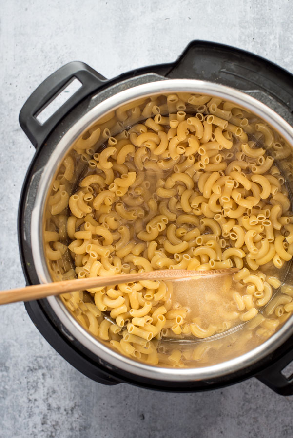 Overhead of macaroni noodles cooking in an Instant pot with a wooden spoon.