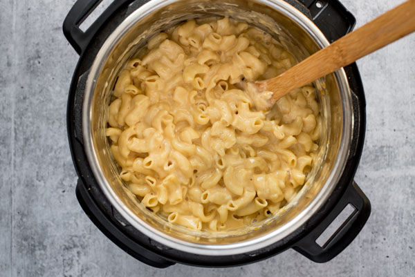 Overhead of creamy homemade pressure cooker macaroni and cheese in an Instant Pot with a wooden spoon.