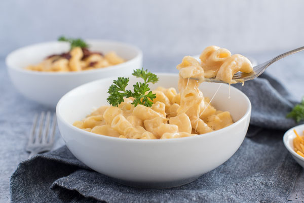 A bowl of creamy homemade pressure cooker macaroni and cheese with a bite being taken out of it with a fork.