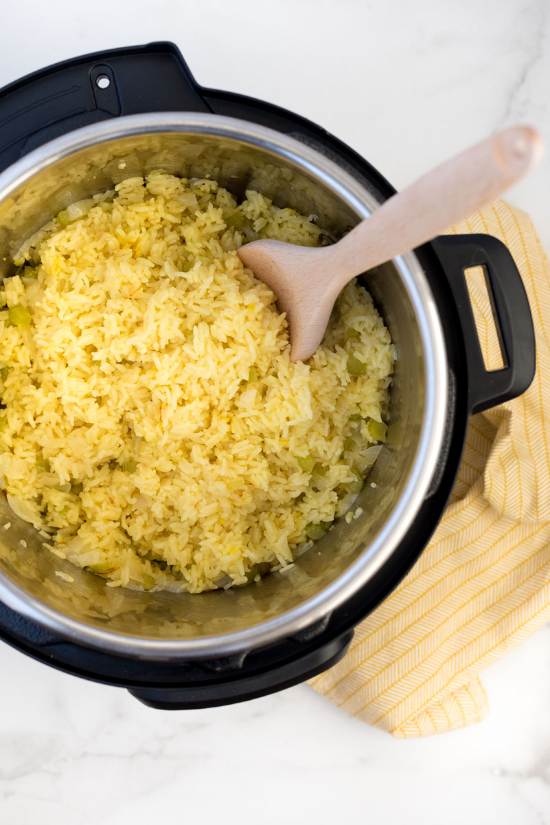 an overhead shot of prepared saffron almond rice pilaf inside an instant pot, with a wooden spoon at the top right