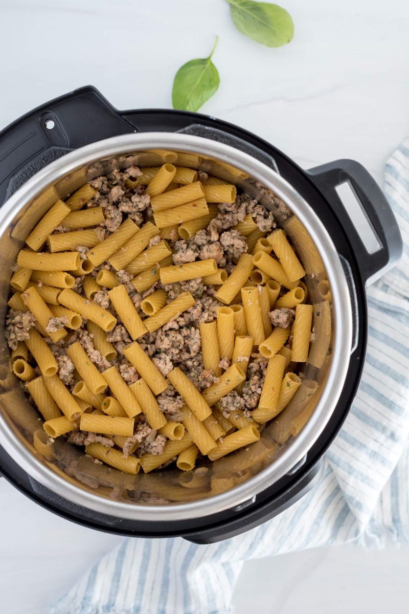 Overhead picture of sausage cooked in an Instant Pot with pasta stirred in and ready to cook.