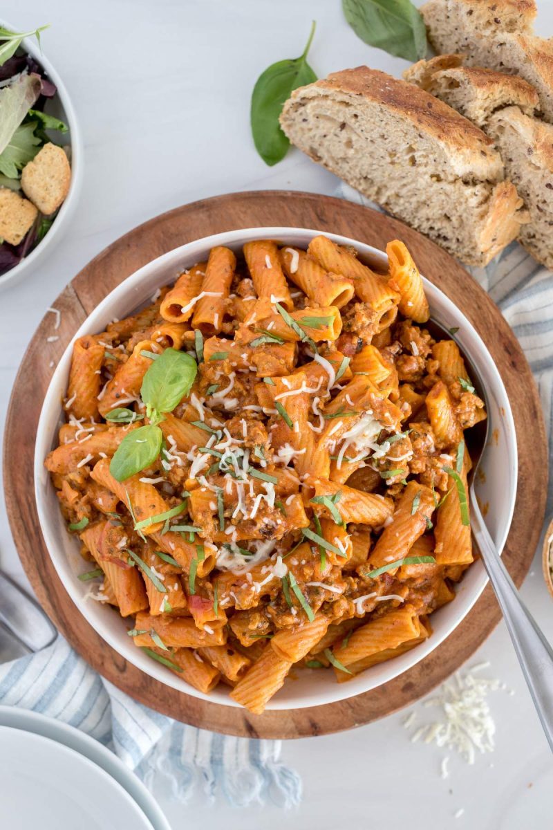 An overhead picture of Instant Pot Rigatoni pasta with sausage in a white bowl topped with cheese and fresh basil.
