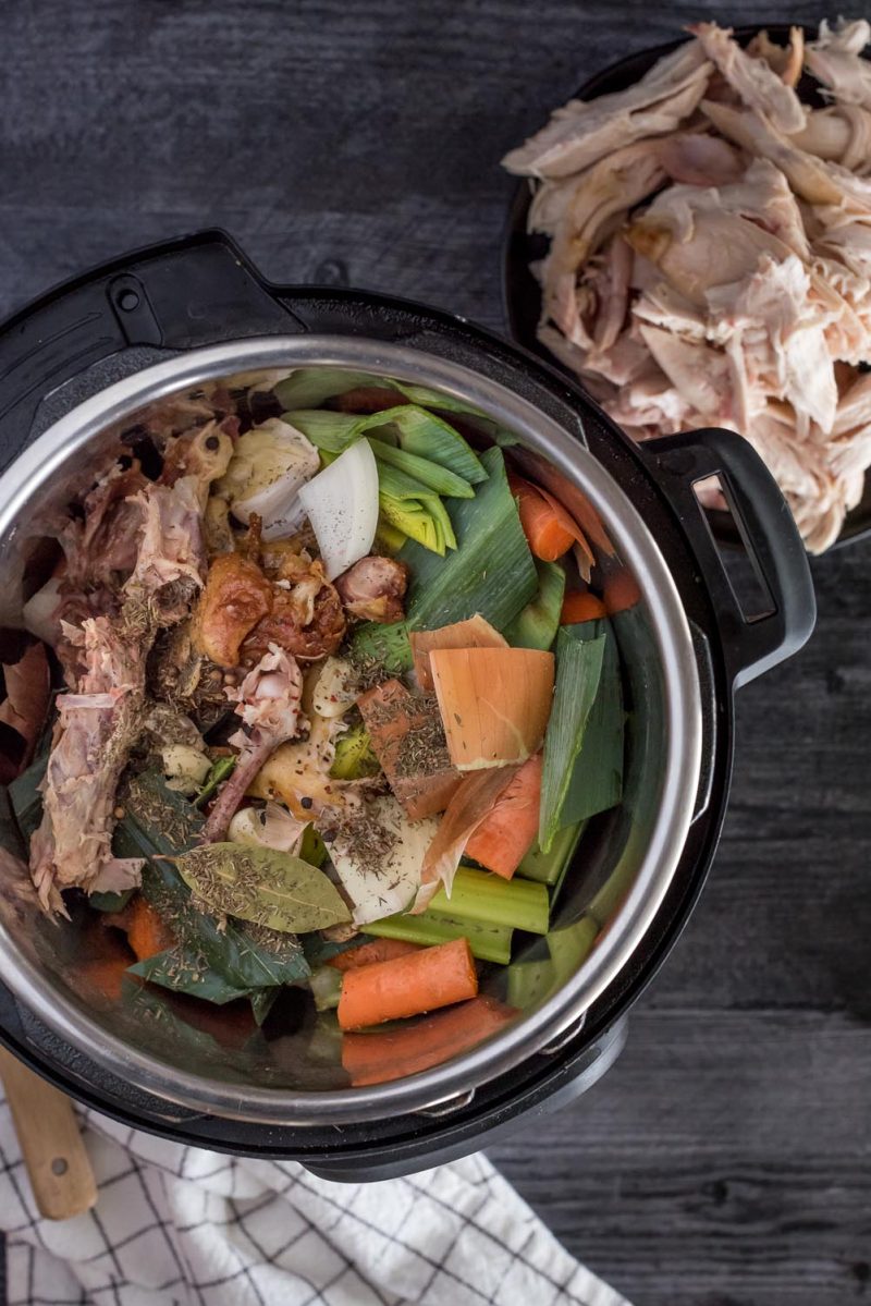 An overhead shot of the chicken bones, veggies, and spices in the Instant Pot ready to pressure cook