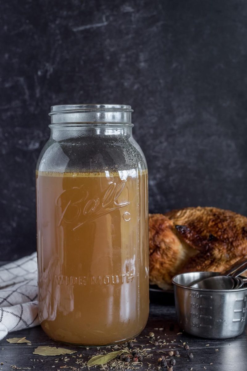 A mason jar filled with chicken broth with a rotisserie chicken in the background