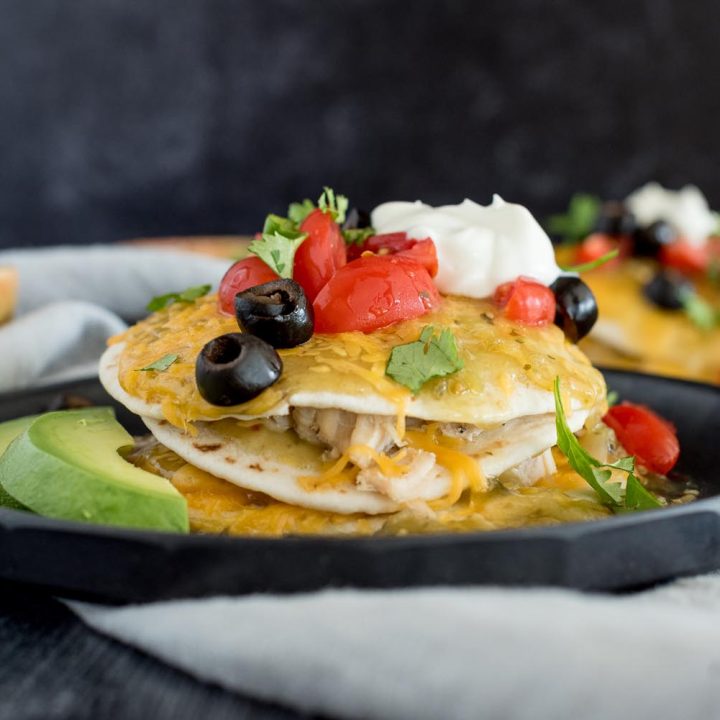 Close up picture of an Instant Pot stacked enchilada topped with olives, tomatoes, cilantro and sour cream, with avocado, cilantro, and tomatoes in the background.