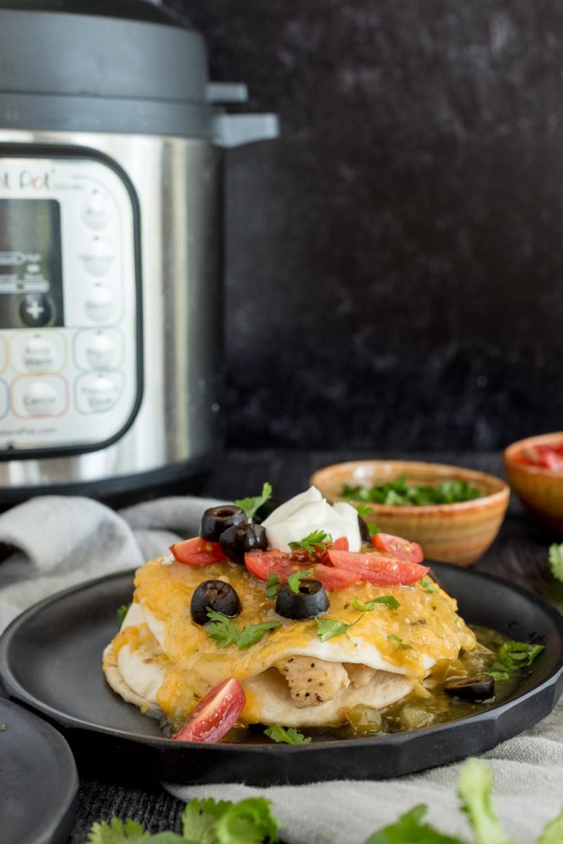 A stacked chicken enchilada topped with olives, tomatoes, sour cream, and placed in front of an Instant Pot.