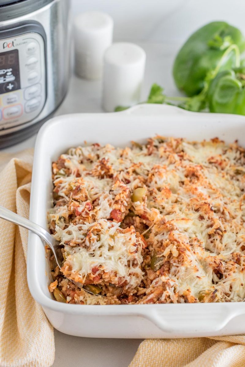 A serving dish with stuffed green pepper casserole with melted cheese on top, placed in front of an Instant Pot.