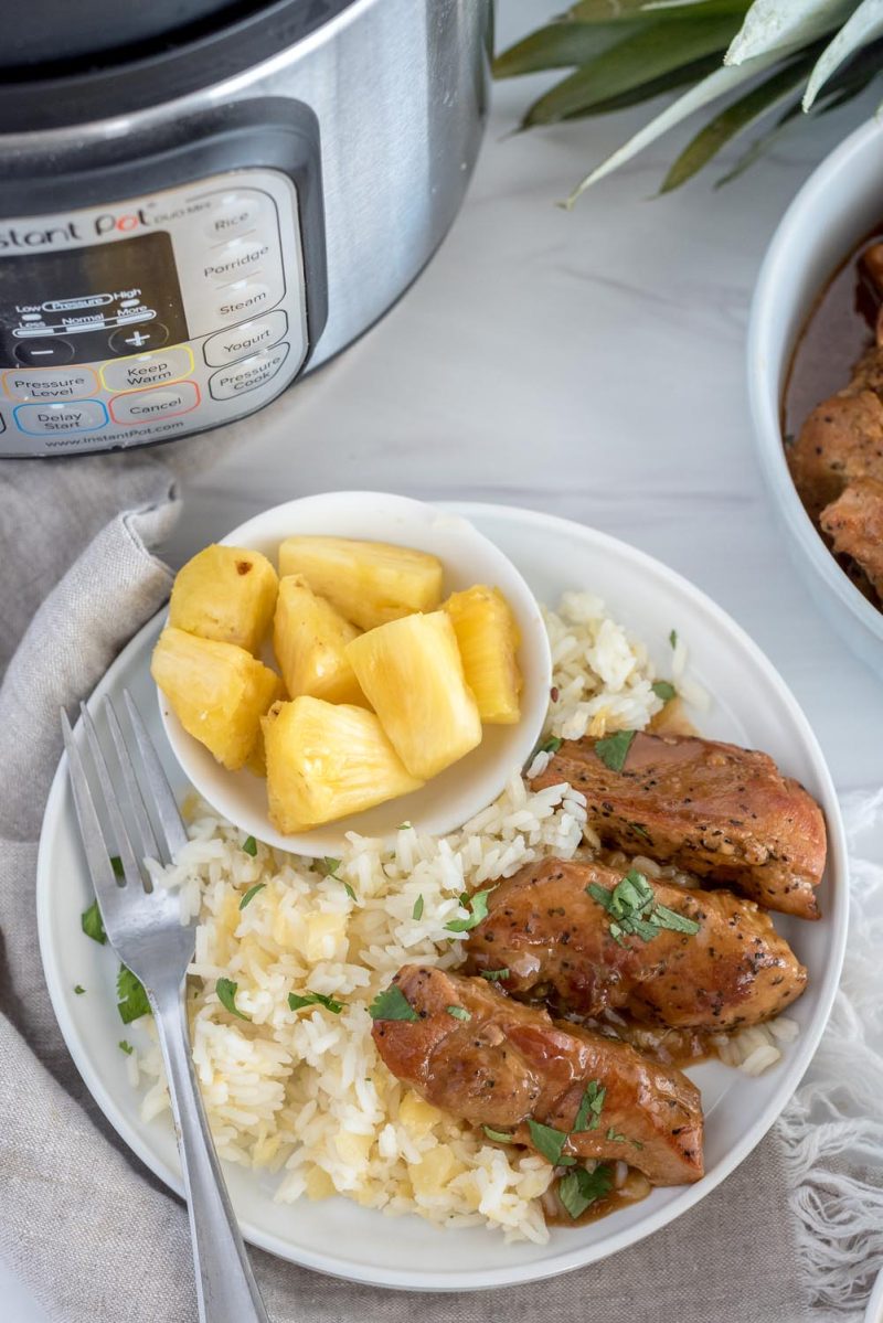 A white plate with sweet and sour country style ribs served with rice and diced pineapple, with an Instant Pot in the background.