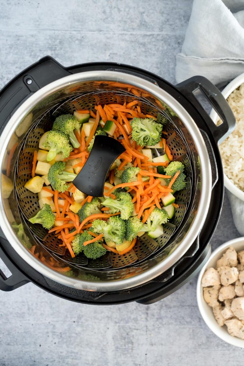 Overhead picture of an Instant Pot with a steamer basket filled with vegetables for teriyaki bowls.