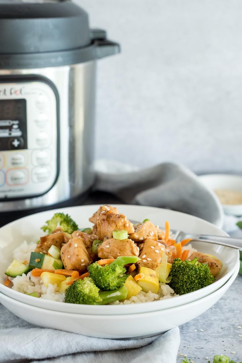 Close up of Instant Pot teriyaki bowls with broccoli, carrots, yellow squash, and green onions, with an Instant Pot in the background.