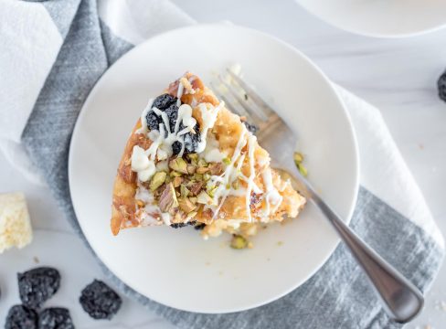 Overhead picture of Insta Pot white chocolate cherry bread pudding on a white plate, iced and topped with chopped pistachios.