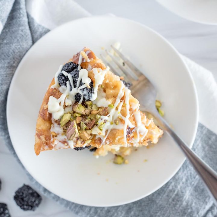 Overhead picture of Insta Pot white chocolate cherry bread pudding on a white plate, iced and topped with chopped pistachios.