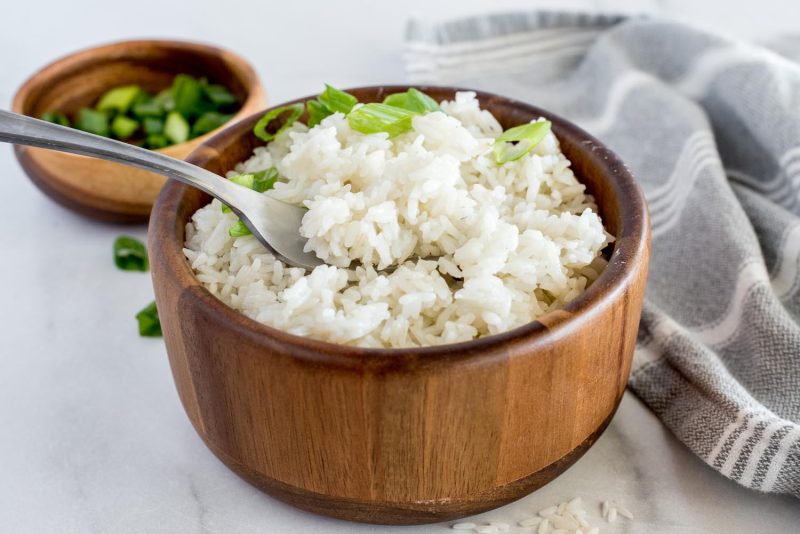 Close up picture of wooden bowl with Instant Pot white rice topped with green onion, with a fork in the bowl.
