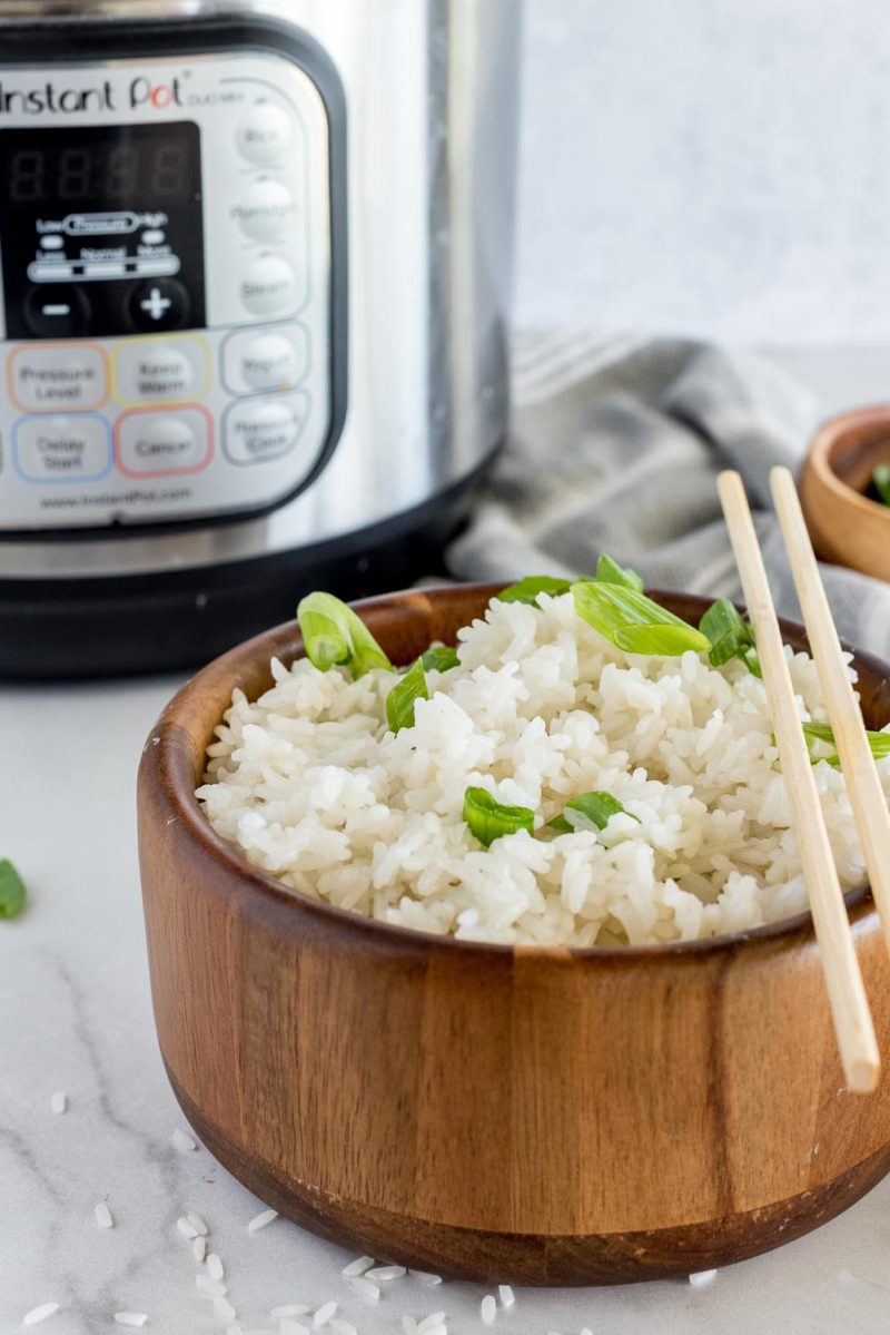 A wooden bowl with white rice topped with green onion, placed in front of an Instant Pot.